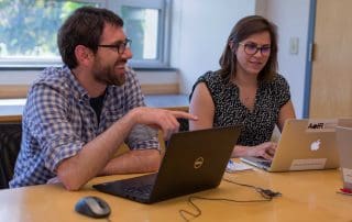 Two faculty members chatting at computers